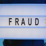 Mãos seguram uma placa com a palavra “fraude” sob iluminação azul.
