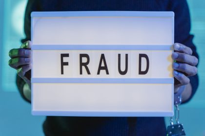 Mãos seguram uma placa com a palavra “fraude” sob iluminação azul.