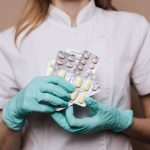 Profissional de saúde usando luvas segura cartelas de medicamentos em ambiente clínico.