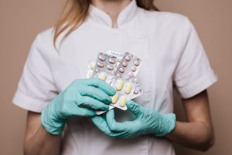 Profissional de saúde usando luvas segura cartelas de medicamentos em ambiente clínico.