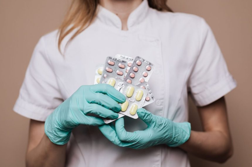 Profissional de saúde usando luvas segura cartelas de medicamentos em ambiente clínico.