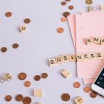 Mesa com moedas, calendário e smartphone exibindo uma calculadora, representando planejamento financeiro para pequenos negócios.