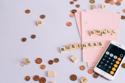 Mesa com moedas, calendário e smartphone exibindo uma calculadora, representando planejamento financeiro para pequenos negócios.