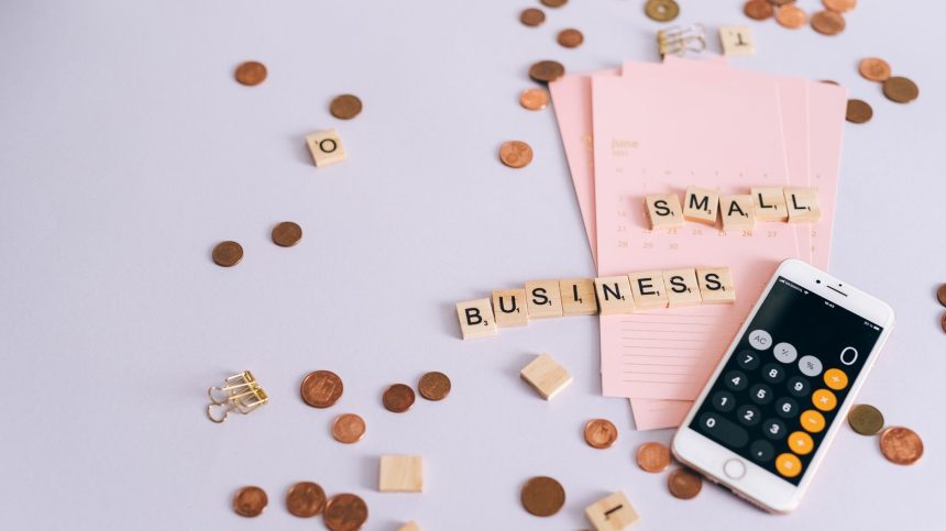 Mesa com moedas, calendário e smartphone exibindo uma calculadora, representando planejamento financeiro para pequenos negócios.